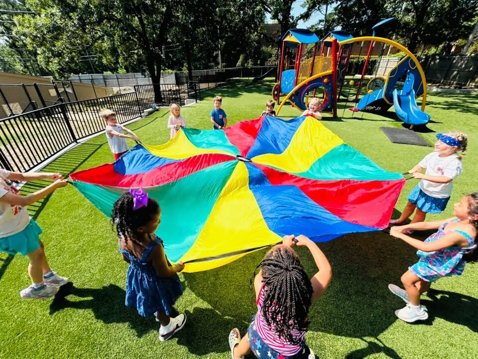 Children at Little Rock Montessori School playing a parachute game together on the playground